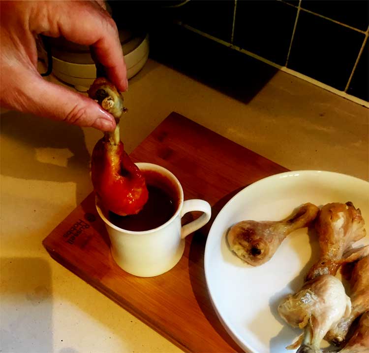 Photo of a hand dipping a chicken leg into spicy sauce.