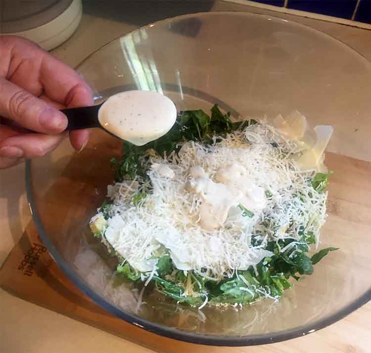photo of hand putting dressing onto Caesar Salad