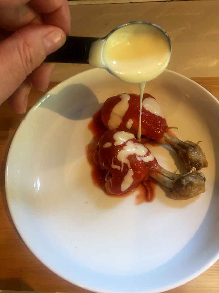 photo of a hand drizzling blue cheese dressing over spicy chicken legs