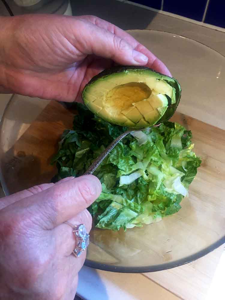 photo of a hand scooping avocado from shell into salad bowl
