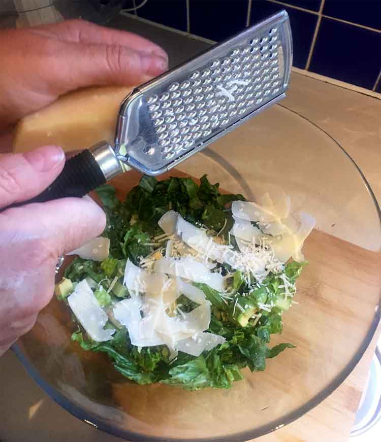 photo of a hand grating cheese onto a caesar salad.