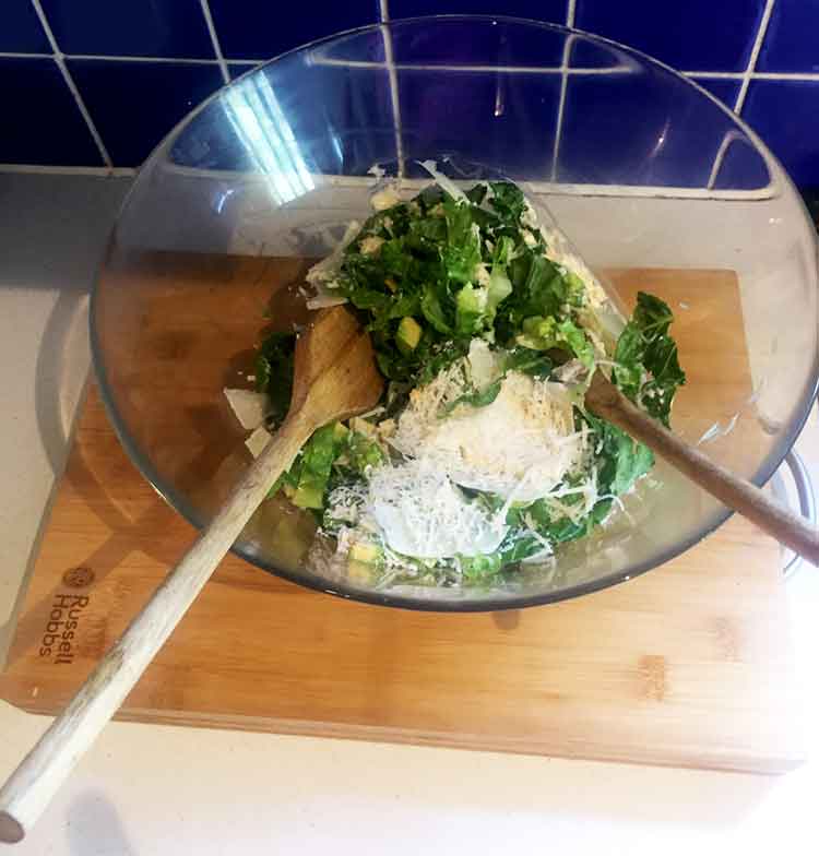 Photo of avocado caesar salad in a glass bowl with salad spoons.